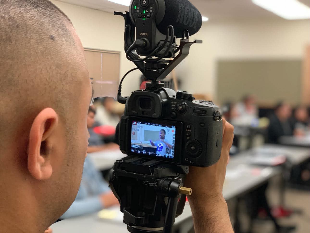 A videographer filming Brian E. Sibley speaking, seen on the camera screen, in a classroom