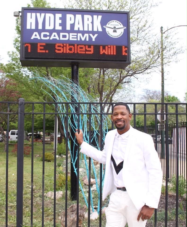 Brian E. Sibley beside the Hyde Park Academy marquee in Chicago showing his name as commencement speaker
